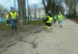 Dzieci w zielonych kamizelkach idą drogą.
