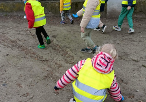Dzieci w zielonych kamizelkach idą drogą.