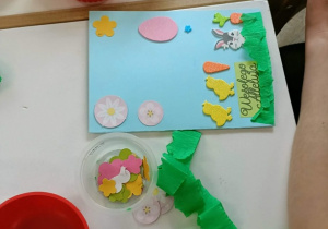 Na stoliku leży wykonywana kartka. Wokół leżą czerwone miseczki.