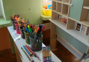 Na stoliku stoją kredki, mazaki i cienkopisy.