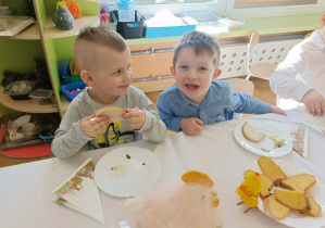 Dwóch chłopców pozuje do zdjęcia. Jeden ma w dłoni chleb.