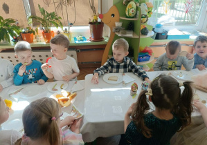 Dzieci siedzą przy stole i jedzą śniadanie.