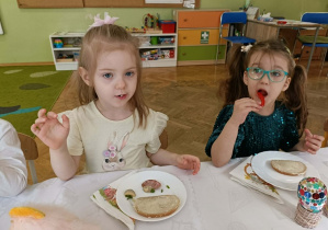 Dwie dziewczynki siedzą przy stole i jedzą śniadanie,