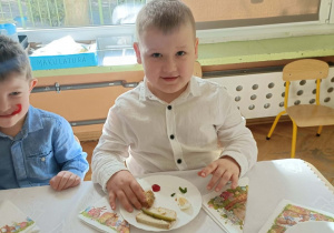 Chłopiec w białej koszuli uśmiecha się do zdjęcia.