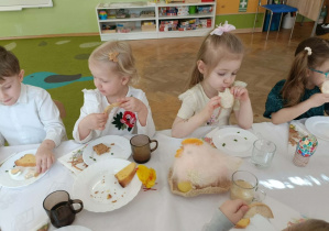 Dzieci siedzą przy stole i jedzą śniadanie.