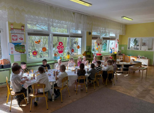 Dzieci siedzą przy długim stole. W tle widać okna.