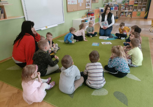 Dzieci siedzą na dywanie z dwiema Paniami.