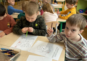Dzieci siedzą przy stoliku i kolorują kolorowanki.