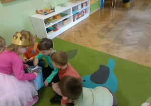Dziewczynka w złotej koronie rozdaje dzieciom cukierki.