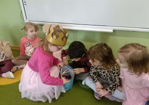 Dziewczynka w złotej koronie rozdaje dzieciom cukierki.