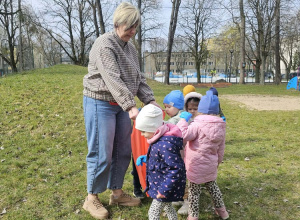 Grupa dzieci stoi z Panią na trawie.