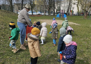 Grupa dzieci stoi z Panią na trawie.