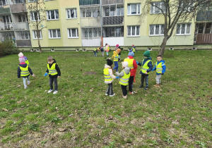 Dzieci chodzą po trawniku i zbierają śmieci.