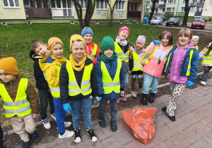 Dzieci stoją na chodniku. Przed nimi leży czerwony worek.