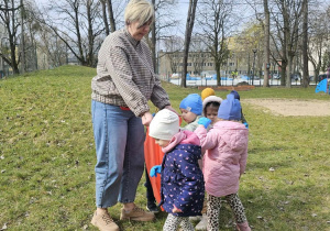 Grupa dzieci stoi z Panią na trawie.