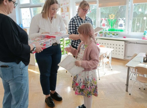 Pani Dyrektor wręcza dziewczynce nagrodę. Po bokach stoją dwie Panie prowadzące.