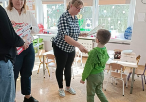 Pani Dyrektor wręcza chłopcu nagrodę. Po bokach stoją dwie Panie prowadzące.