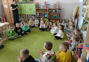 Grupa dzieci siedzi na zielonym dywanie.