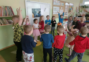 Dziewczynka w koronie siedzi w środku koła. Dzieci wokół niej tańczą.