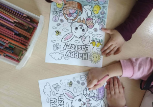 Dzieci kolorują kolorowankę z zajączkiem i jajkami.