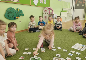 Dziewczynka w różowych okularach siedzi na zielonym dywanie i segreguje odpady.