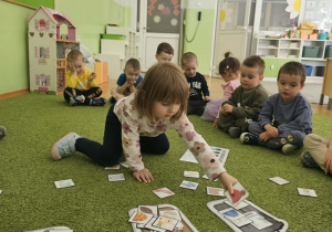 Dziewczynka w bluzce w kwiatki siedzi na zielonym dywanie i segreguje odpady.