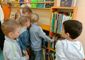 Piątka chłopców szuka książek na regale.