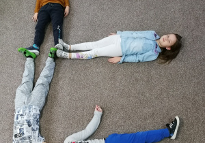 dzieci tworzą literkę E leżąc na dywanie