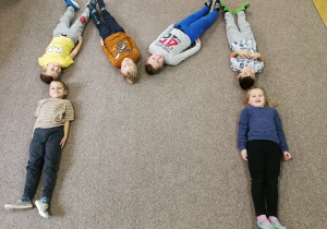 kształt literki M - dzieci leżące na dywanie