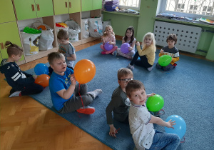 dzieci siedzą na dywanie z kolorowymi balonami