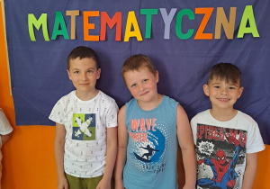 trzech chłopców na tle tablicy z napisem olimpiada matematyczna