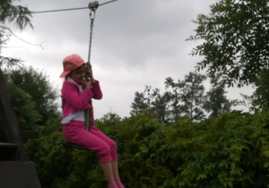 Dziewczynka w różowym stroju i czapce zjeżdża na tyrolce