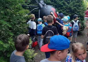 Grupka dzieci ogląda i dotyka ogromnego czarnego pająka z czerwonym krzyżykiem