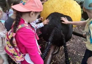 Grupka dzieci ogląda i dotyka gigantyczna pszczołę pokryta czarnym i białym futerkiem