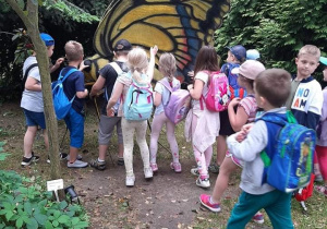 Grupka dzieci dotyka ogromnego żółto czarnego motyla pokrytego prawdziwa skórą ze zwierzęcia