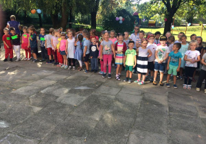 dzieci śpiewają Hymn Przedszkolaka w ogrodzie przedszkolnym, słoneczna pogoda, w tle kolorowe balony i dekoracje