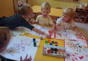 Dzieci siedzą przy stolikach i malują palcami kropkowe dzieła
