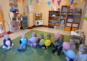 Dzieci siedzą na dywanie z kolorowymi balonami