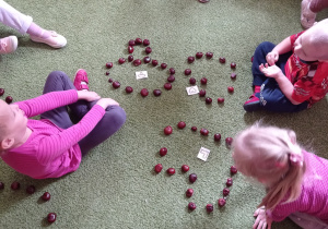 Dzieci siedzą na dywanie i układają wzory z kasztanów