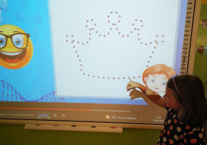 Dziewczynka przy tablicy multimedialnej łączy kropki we wzór