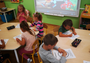 Dzieci przy stolikach kolorują kropki w tle tablica multimedialna