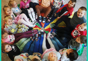 Dzieci siedzą na kolorowej chuście i uśmiechają się do zdjecia