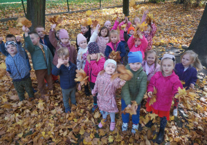 Grupa dzieci w ogrodzie przedszkolnym pozuje do zdjęcia podczas zabawy liśćmi