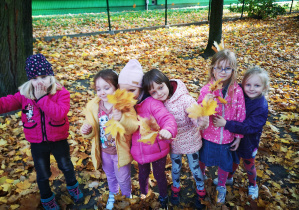 Grupa dzieci w ogrodzie przedszkolnym pozuje do zdjęcia podczas zabawy liśćmi