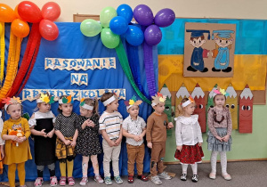 Grupa dzieci pozuje do zdjecia, w tle dekoracja pasowanie na przedszkolaka i balony