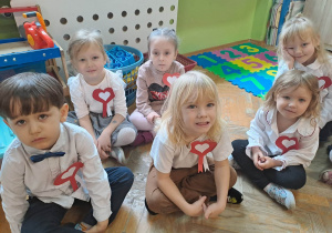 Dzieci siedzą na podłodze, na piersi mają kotylion w barwach narodowych