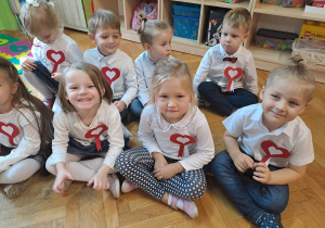 Dzieci siedzą na podłodze, na piersi mają kotylion w barwach narodowych