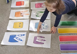 Dzieci siedzą na dywanie, dziewczynka dopasowuje obrazek do odpowiedniego koloru
