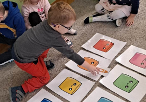 Dzieci siedzą na dywanie, chłopiec dopasowuje obrazek do odpowiedniego koloru