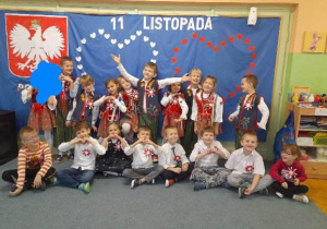 Grupa dzieci pozuje do zdjęcia na tle dekoracji patriotycznej